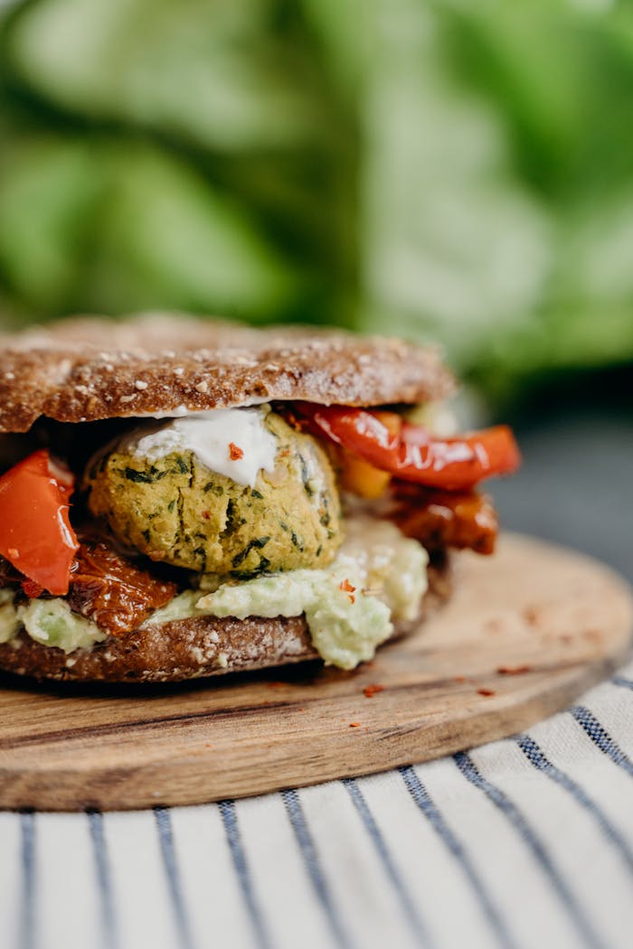 A close-up of a delicious vegan falafel burger with fresh vegetables on a rustic wooden plate.